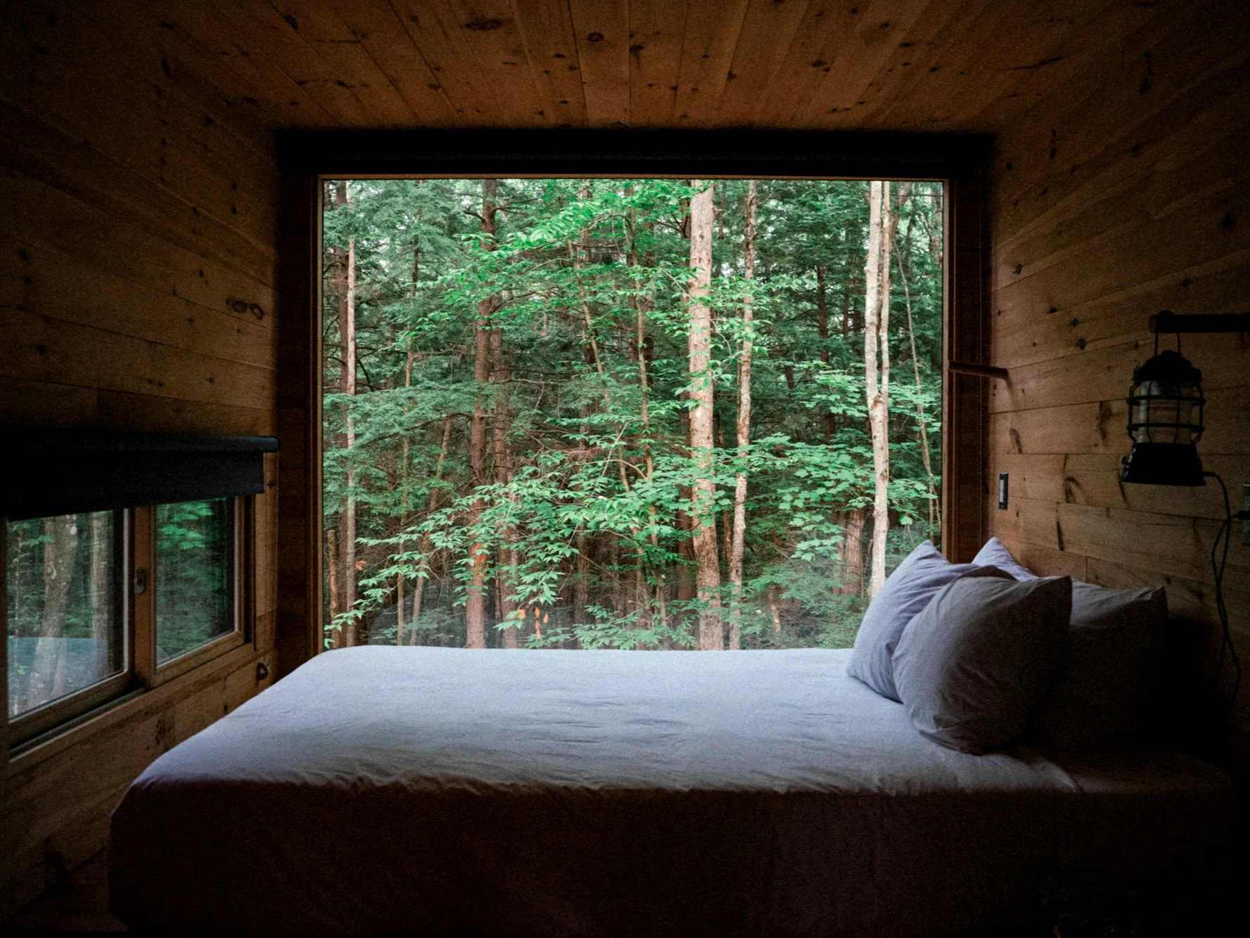 Dormitorio de alojamiento glamping con gran ventanal al bosque